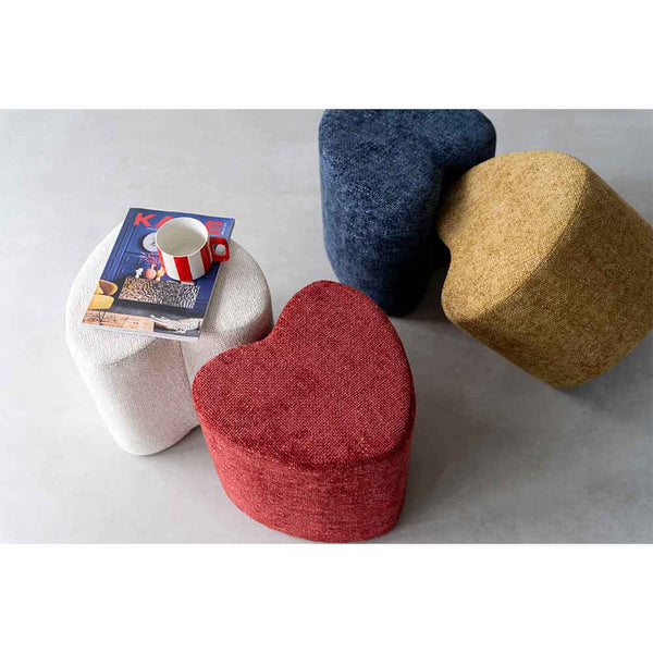 Vier herzförmige Hocker in Weiß, Rot, Blau und Gelb. Auf dem weißen Hocker stehen eine Tasse und eine Zeitschrift.