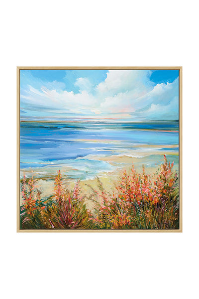 Ein gerahmtes Bild zeigt einen Sandstrand mit orangefarbenen Blumen im Vordergrund, ruhiges blaues Wasser in der Mitte und einen hellen Himmel mit Wolken darüber.