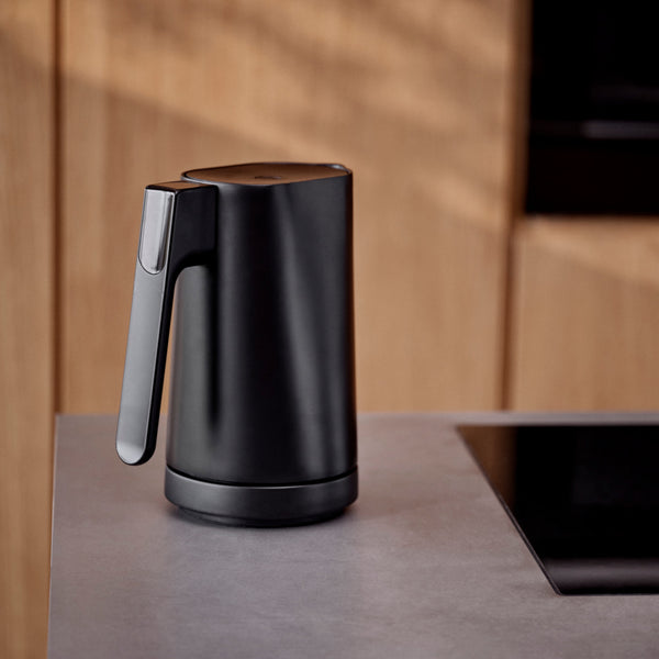 Ein eleganter schwarzer Wasserkocher steht auf einer modernen Küchenzeile mit Holzschränken im Hintergrund.