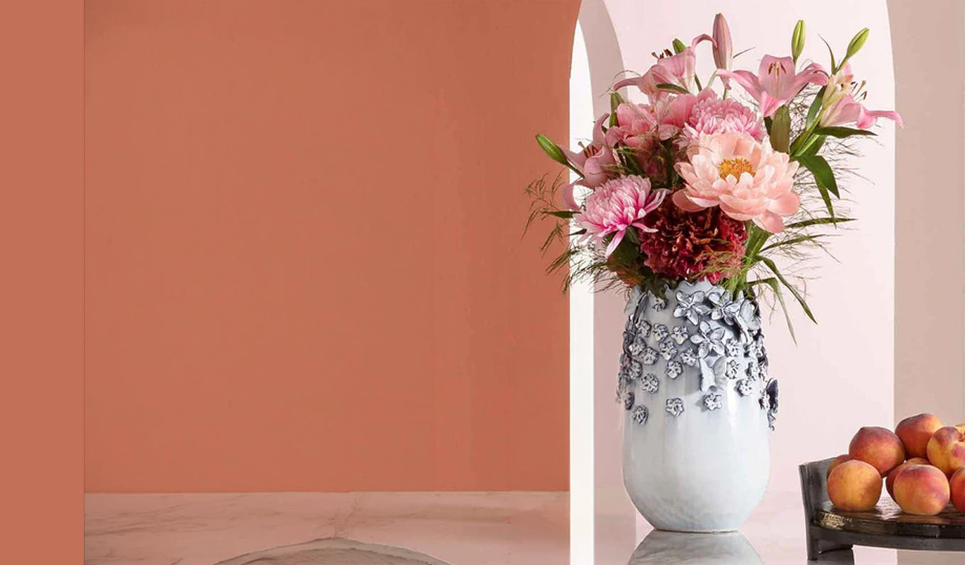 Hellblaue Keramikvase mit rosafarbenen Blumenstrauß mit Obstschale gefüllt mit aprikosen