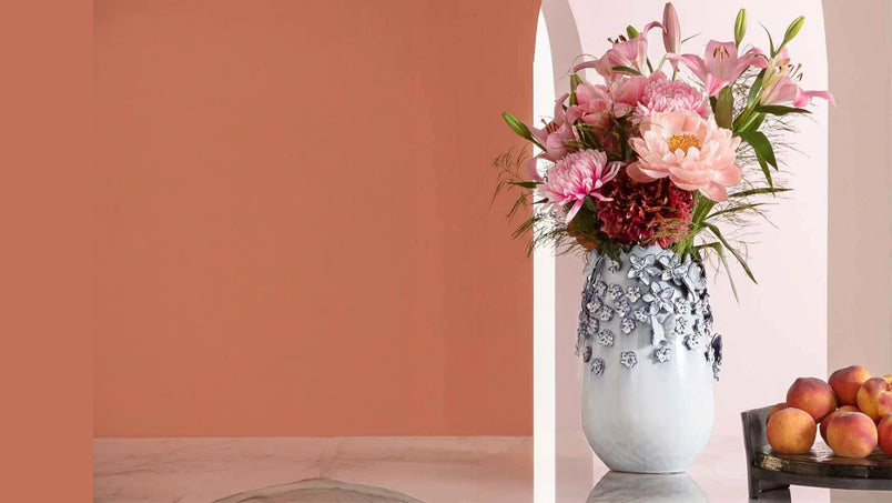 Hellblaue Keramikvase mit rosafarbenen Blumenstrauß mit Obstschale gefüllt mit aprikosen