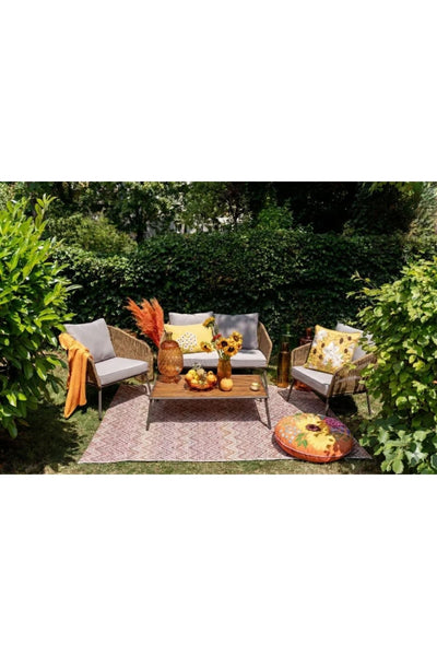 Terrassenmöbel mit einem Sofa, zwei Stühlen und einem Couchtisch auf einem gemusterten Teppich, umgeben von Grün und dekoriert mit Blumen, Kissen und herbstlichen Motiven.