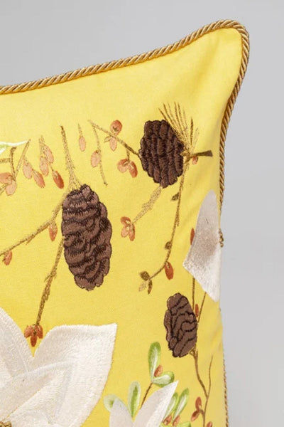Nahaufnahme eines gelben Kissens mit gestickten Tannenzapfen, Zweigen und Blättern und einer gedrehten Kordel entlang des Randes.