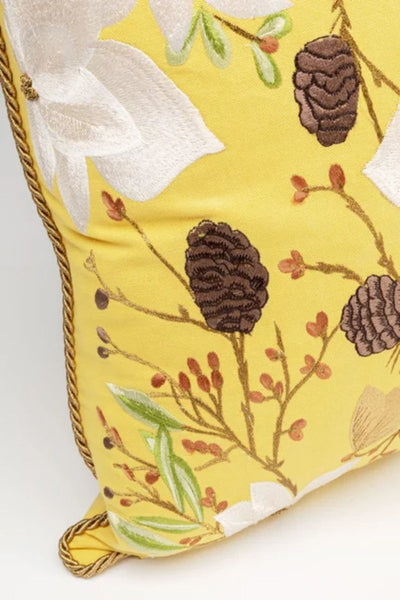 Gelbes Dekokissen mit gestickten Tannenzapfen, weißen Blüten und grünen Blättern und einem gedrehten Seil am Rand.