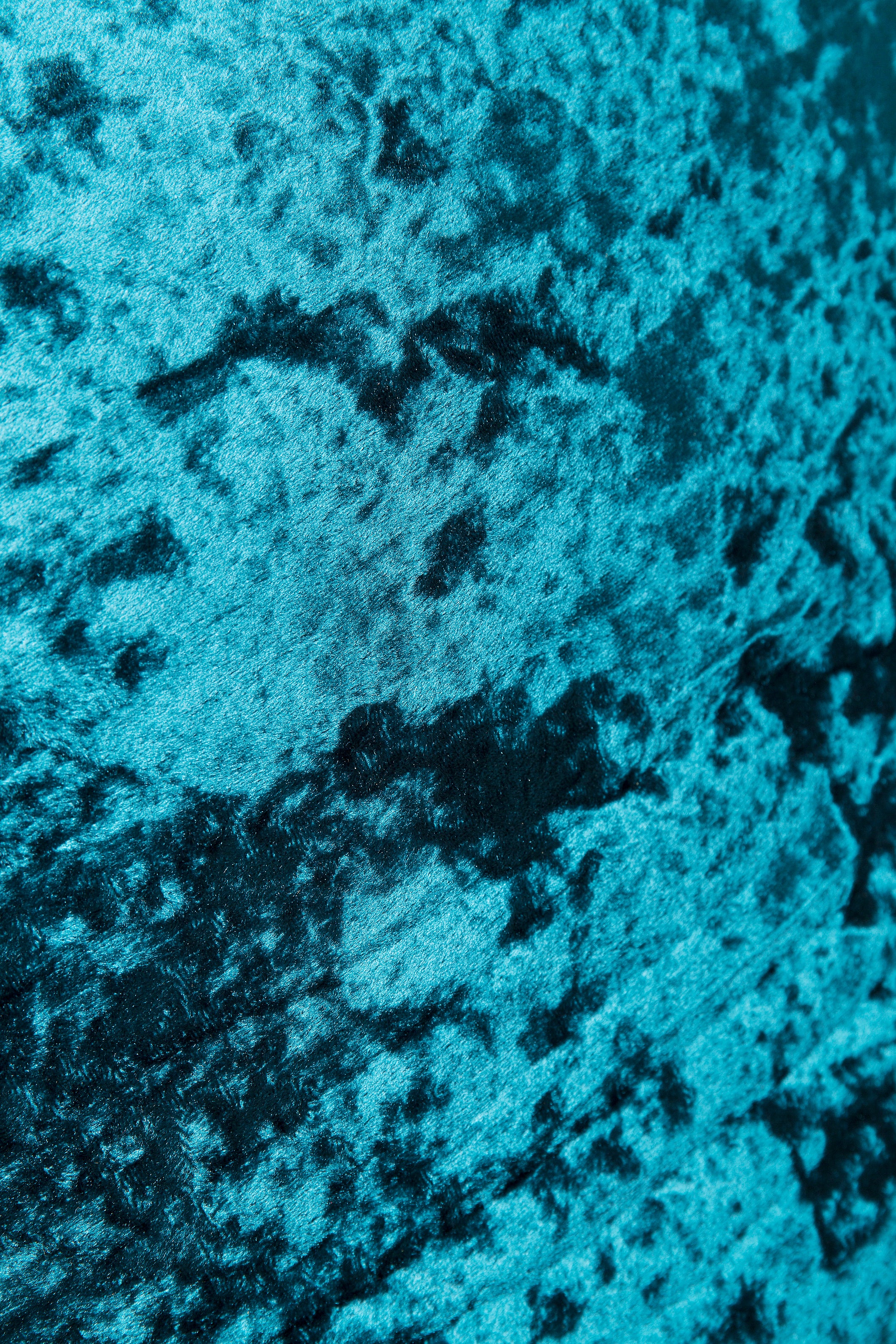 Nahaufnahme eines blauen, zerknitterten Samtstoffs mit weicher, strukturierter und gesprenkelter Optik.