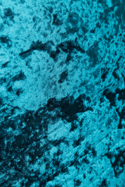 Nahaufnahme eines blauen, zerknitterten Samtstoffs mit weicher, strukturierter und gesprenkelter Optik.