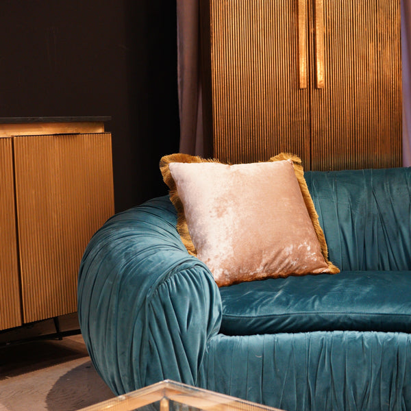 Tealfarbenes Samtsofa mit goldfarbenen Kissen neben goldenen Schränken in einem modernen Wohnzimmer.