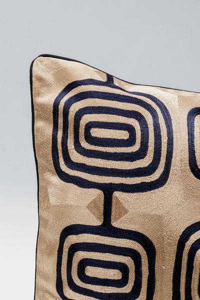 Ein goldenes Kissen mit einem schwarzen geometrischen Muster auf hellgrauem Hintergrund.