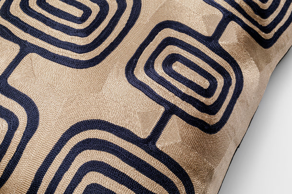 Beigefarbenes Kissen mit einem geometrischen, marineblauen, quadratischen Muster auf strukturiertem Stoff.