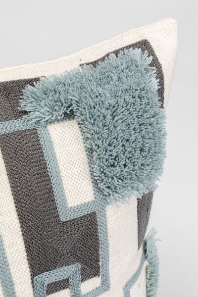 Nahaufnahme eines dekorativen Kissens mit strukturierten blauen und schwarzen geometrischen Mustern und getufteten blauen Akzenten.