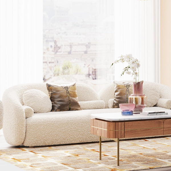 Cremefarbenes Sofa mit strukturierten Kissen, Couchtisch aus Holz und Vase mit Blumen in einem hellen, luftigen Wohnzimmer.