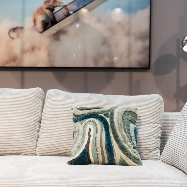 Ein beiges Sofa mit einem gemusterten Kissen vor einem gerahmten Foto eines fliegenden Flugzeugs an der Wand.