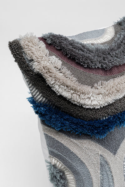 Nahaufnahme eines Kissens mit strukturiertem, mehrfarbigem, geschichtetem Stoff in Grau-, Blau-, Beige- und Schwarztönen.