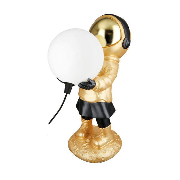 Goldene Astronautenfigur, die eine runde weiße Lampe hält, auf einem strukturierten Sockel steht und ein sichtbares Stromkabel hat.