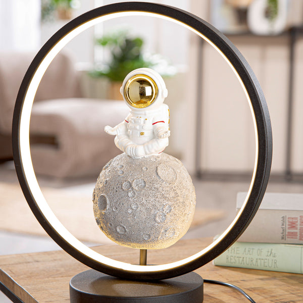 Eine runde Lampe mit einer kleinen Astronautenfigur, die auf einer mondähnlichen Kugel im Inneren des Rings sitzt.
