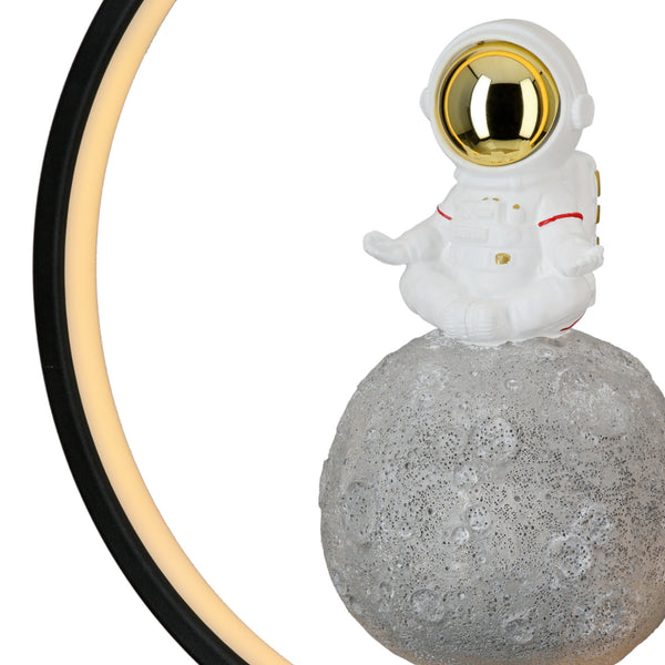 Eine kleine Astronautenfigur sitzt auf einem strukturierten Mond mit einer runden LED-Leuchte daneben.