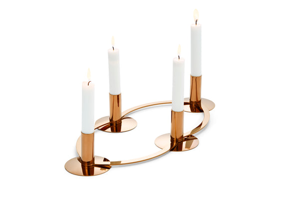 Vier brennende weiße Kerzen in einem modernen, runden goldenen Metallkerzenhalter auf weißem Hintergrund.