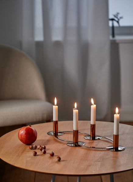 Vier brennende Kerzen, ein Granatapfel und Haselnüsse auf einem Holztisch in einem gemütlichen Raum mit einem Stuhl und einem Fenster.