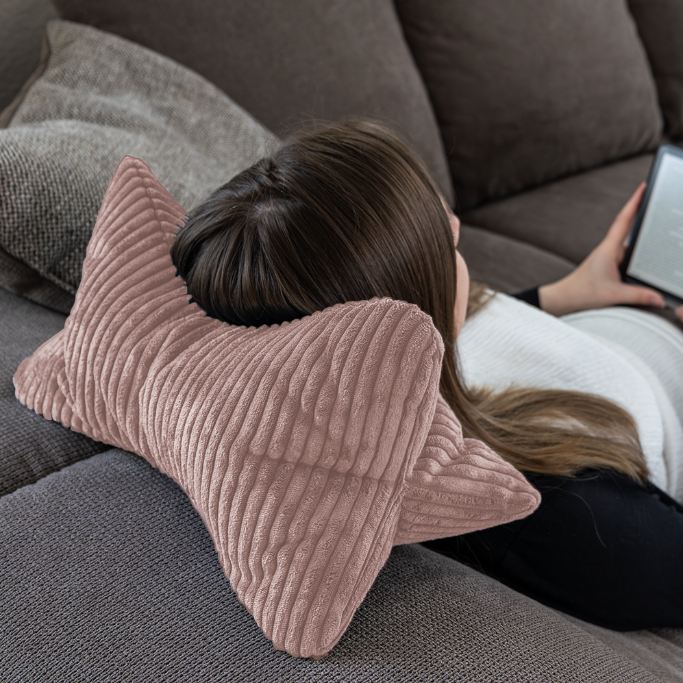 Eine Frau entspannt sich auf einer Couch, legt ihren Kopf auf den Leseknochen Cozy Shara - Rose und liest dabei auf einem E-Reader.