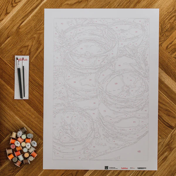 Ein Malset mit einer Leinwand, Farbtöpfen und zwei Pinseln, die auf einem Holzboden angeordnet sind.