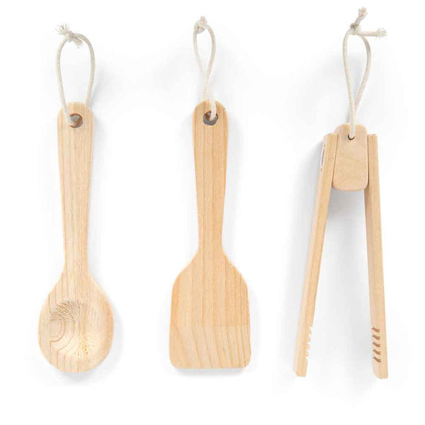 Drei hölzerne Küchenutensilien - Löffel, Pfannenwender und Zange - hängen vertikal an Schnüren vor einem weißen Hintergrund.