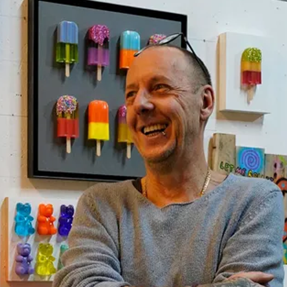 Abbildung des Künstlers Michael Pfannschmidt mit einem Kunstwerk im Hintergrund auf dem Eis am Stil Objekte sowie Gummibärchen gezeigt werden 