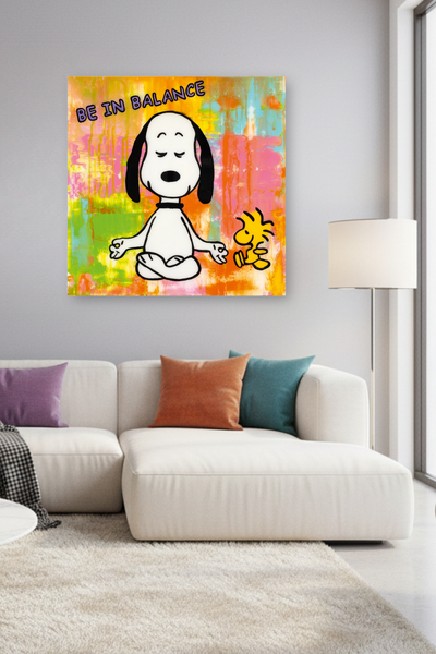 Über einer Couch im Wohnzimmer hängt ein farbenfrohes Kunstwerk: Snoopy sitzt im Schneidersitz mit geschlossenen Augen und meditiert gemeinsam mit Woodstock vor einem abstrakten Hintergrund, über dem die Worte BE IN BALANCE stehen.