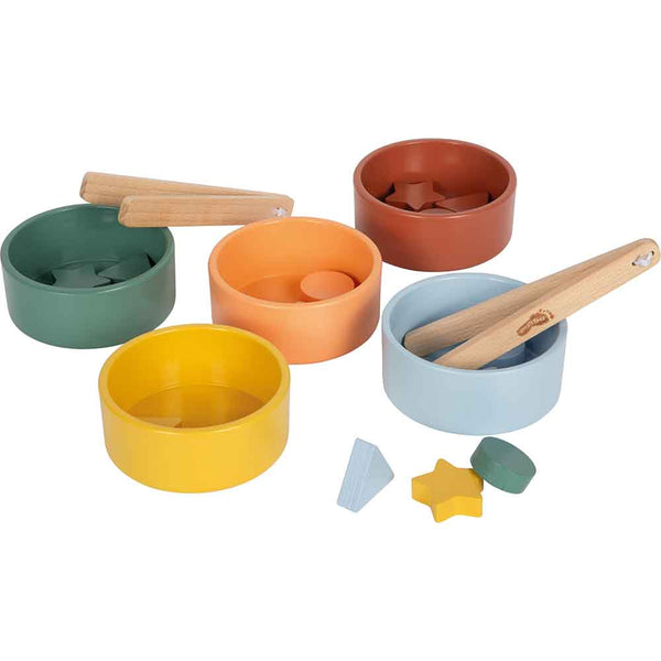 Fünf farbige Schalen, jede mit einer anderen Form im Inneren, zwei Holzzangen und verschiedene kleine geometrische Formen, die in der Nähe verstreut sind.