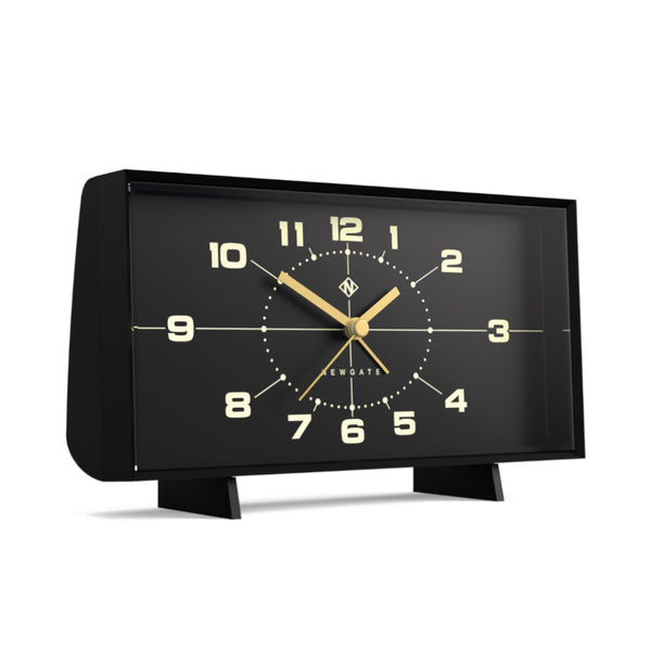 Schwarze rechteckige Analoguhr mit goldenen Zeigern und Zahlen auf schwarzem Zifferblatt, die auf zwei kleinen Beinen steht.