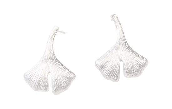 Silberne Ohrringe in Form von Ginkgoblättern mit strukturierten, detaillierten Oberflächen auf weißem Hintergrund.