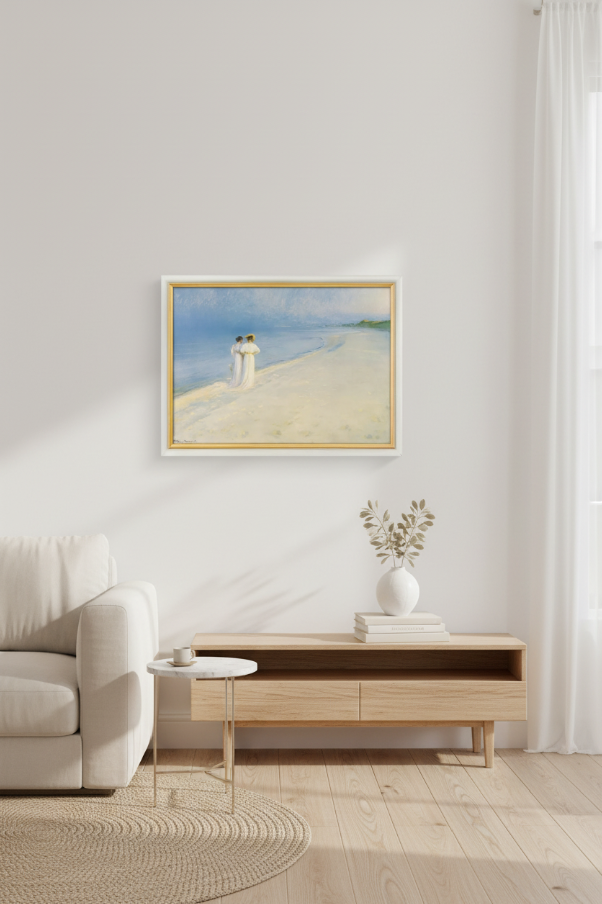 Ein minimalistisches Wohnzimmer mit einem weißen Sofa, einem kleinen runden Tisch und einer Holzkonsole unter einem gerahmten Strandbild an einer weißen Wand. Licht fällt durch ein Fenster mit weißen Vorhängen ein.