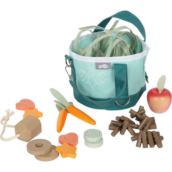 Eine blaugrüne Stofftasche mit Spielzeuggemüse, einem Holzapfel, einer Karotte und verschiedenen geformten Holzteilen, die um sie herum angeordnet sind.