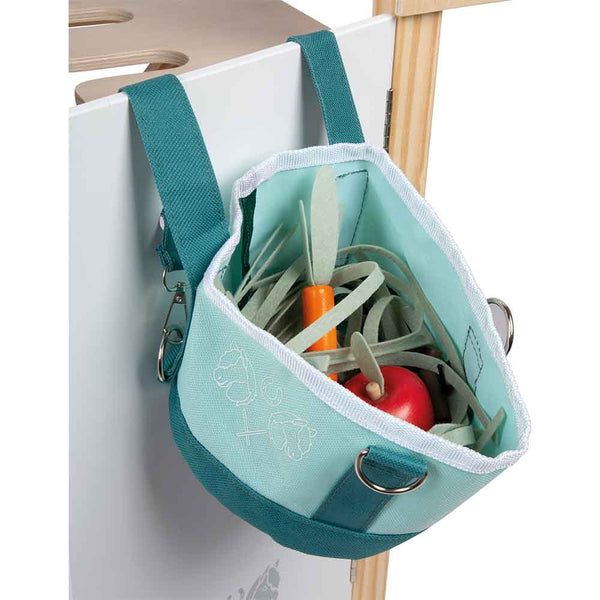 Ein Stoffbeutel, gefüllt mit Spielzeuggemüse, hängt an einem Haken auf einer weißen Fläche.