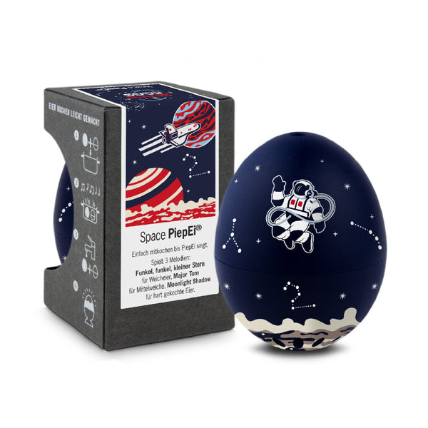 Eine dunkelblaue, eiförmige Zeitschaltuhr mit Astronauten- und Sternbildmotiven, daneben eine Schachtel mit Grafiken zum Thema Weltraum und Produktinformationen.