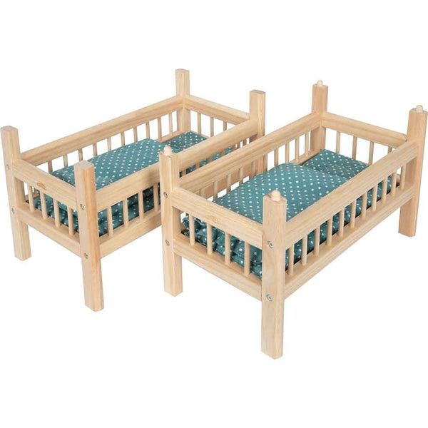 Zwei kleine Puppenbetten aus Holz mit grüner Tupfenbettwäsche, nebeneinander auf weißem Hintergrund.