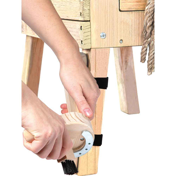 Eine Person reinigt mit einer handgeführten Holzbürste das Bein eines Holztisches oder einer Holzbank.