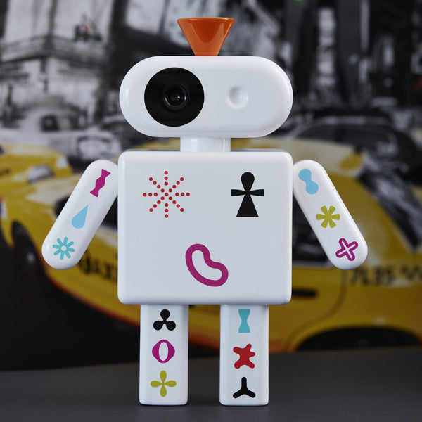 Spielzeugroboter mit bunten Symbolen steht vor einem verschwommenen gelben Auto und einer Stadtstraße im Hintergrund.