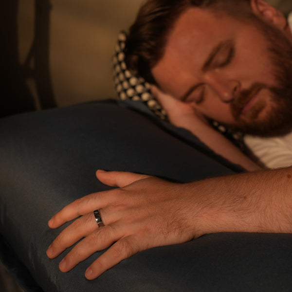 Ein bärtiger Mann schläft auf einem blauen Kissen, seine Hand mit einem Ring liegt sanft auf dem Kissen.