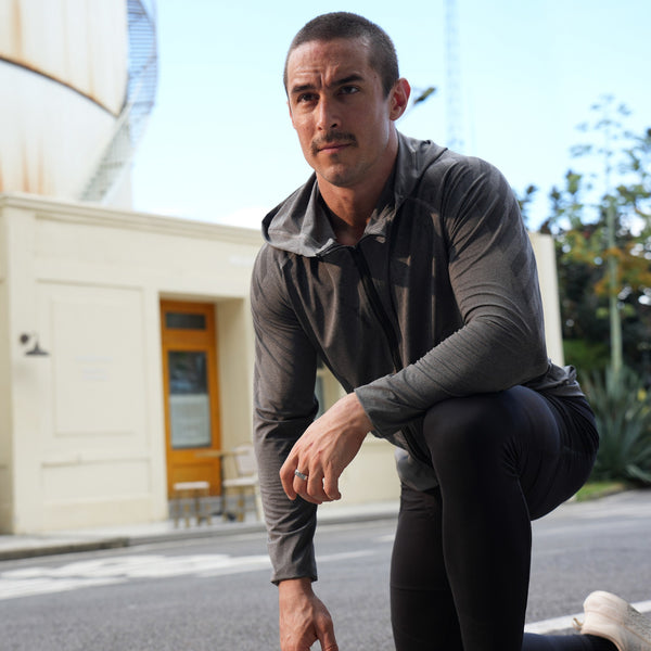 Mann in Sportkleidung kniet im Freien auf der Straße und bereitet sich auf einen Lauf vor, mit Gebäuden im Hintergrund. Er trägt den Smart Ring an seiner linken Hand 