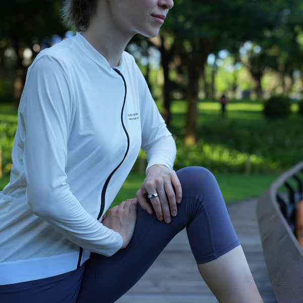 Frau in Sportkleidung dehnt sich auf einem Holzweg in einem grünen Park mit Bäumen im Hintergrund. Sie trägt den Smart Rind an der linken Hand 