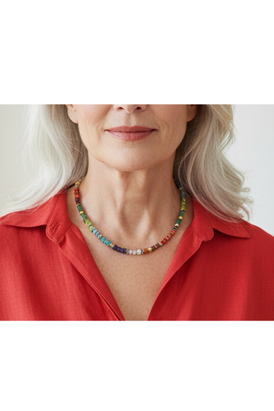 Bunte Perlenkette mit quadratischen und scheibenförmigen Perlen in verschiedenen Farben und einem goldenen Verschluss, getragen am Hals einer älteren Dame in roter Bluse. 