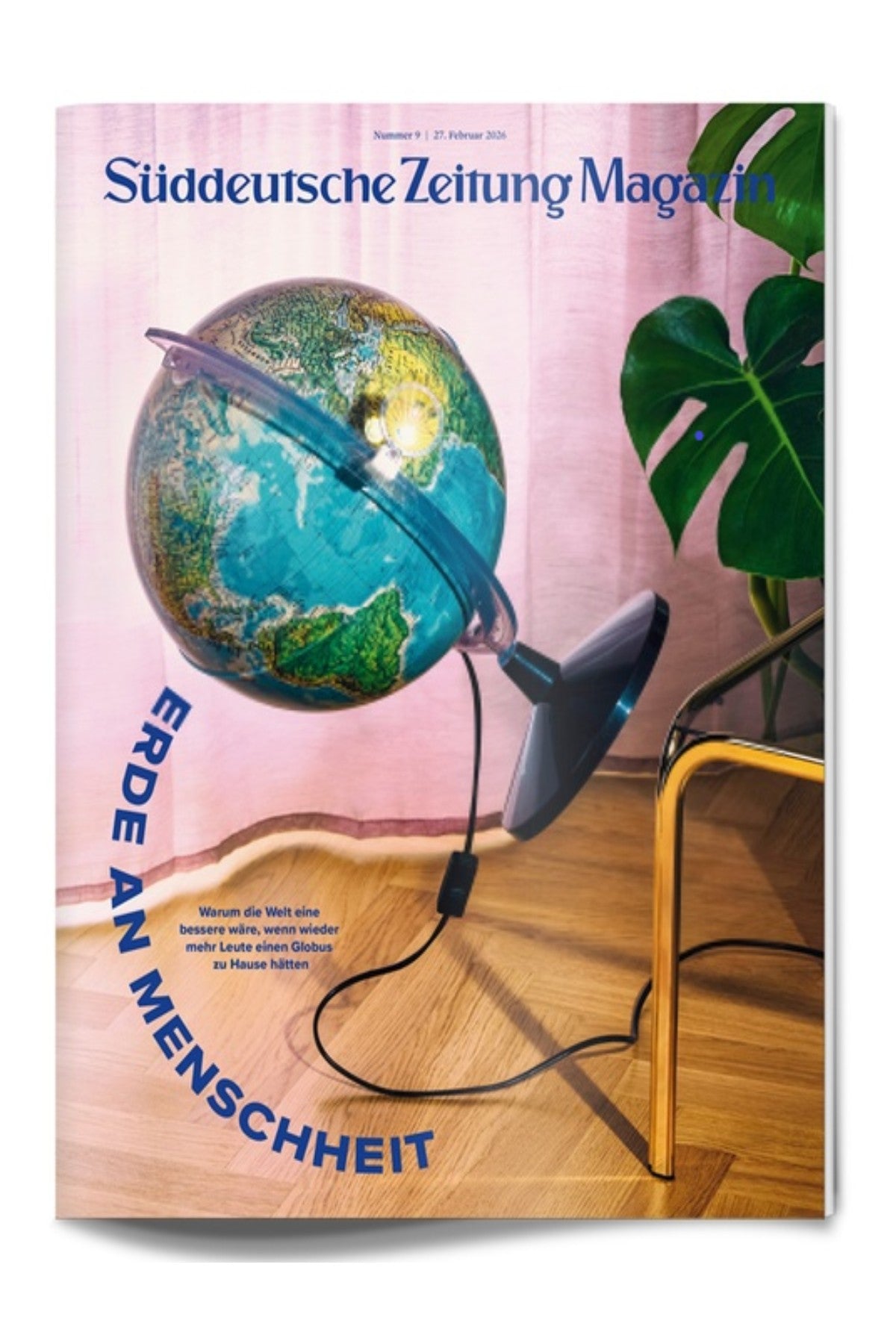 Eine geneigte Erdkugellampe auf einem Ständer ist eingesteckt und wirft Licht in ein Wohnzimmer mit rosa Vorhängen, einem goldenen Stuhl und einer grünen Pflanze. Der Text auf dem Cover einer deutschen Zeitschrift überlagert das Bild.