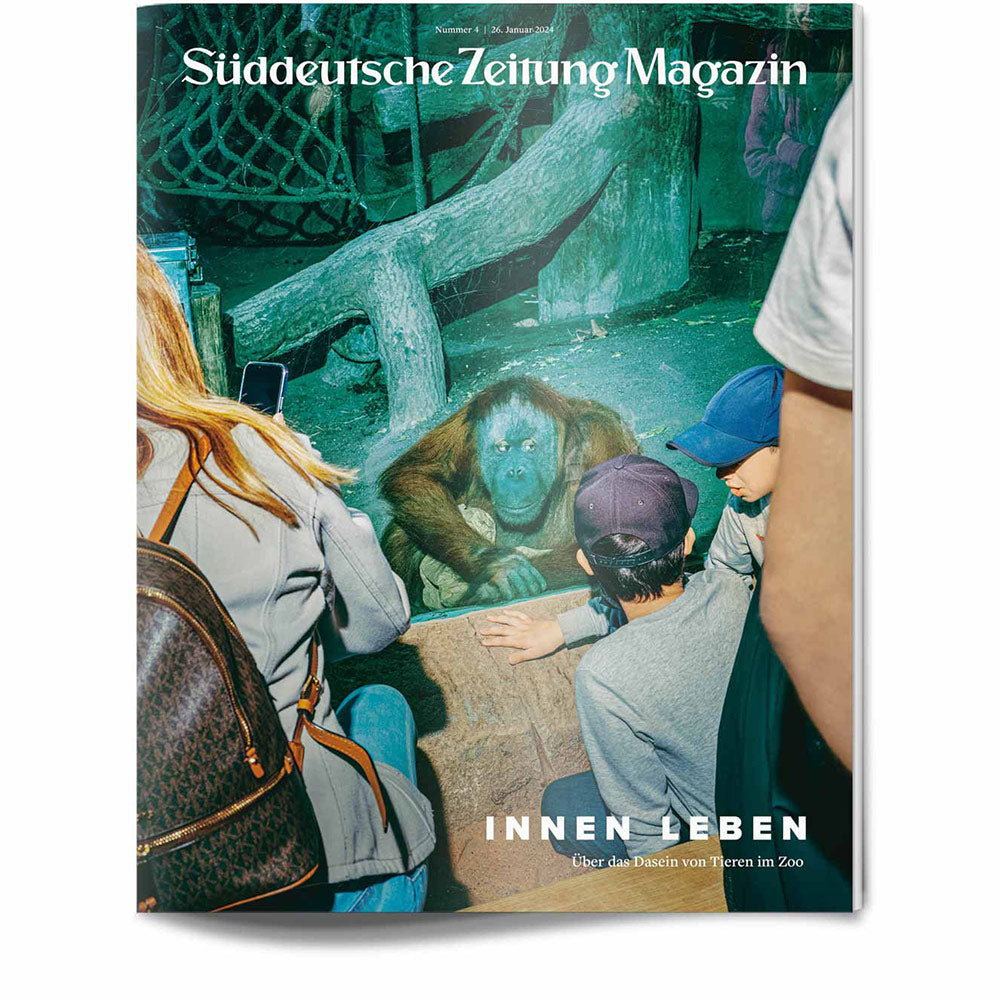 Mehrere Personen beobachten einen Orang-Utan, der in einem Zoo hinter Glas sitzt; Text auf der Titelseite der Zeitschrift.