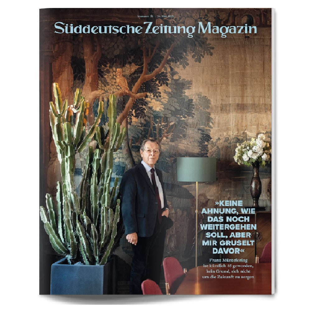 Ein Mann im Anzug steht in einem Innenraum neben einem großen Kaktus und einer Lampe, mit einem Wandteppich und dem Titeltext des Süddeutsche Zeitung Magazins.