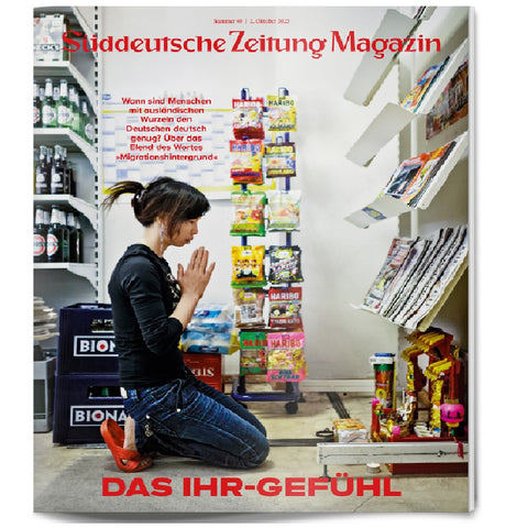 Eine Frau kniet und betet in einem Ladengang, der von Regalen mit Snacks und Zeitschriften gesäumt ist.