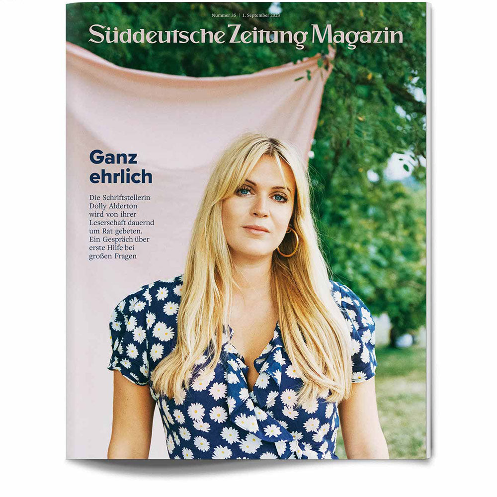 Eine Frau in einem blauen Blumenkleid steht im Freien vor einem rosa Stoffhintergrund auf einem Zeitschriftencover.