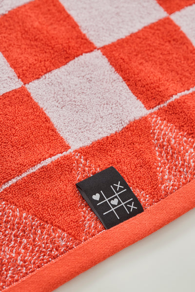 Rot-weiß kariertes Handtuch mit schwarzem Anhänger, der ein Tic-Tac-Toe-Muster und ein kleines Herzsymbol zeigt.