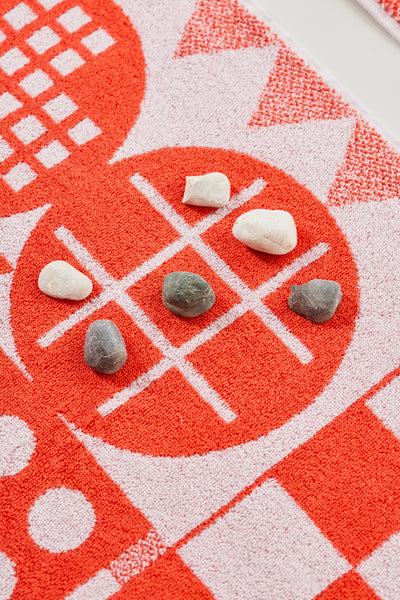 Sechs kleine Steine auf einem rot-weißen Tic-Tac-Toe-Brett mit geometrischen Mustern.