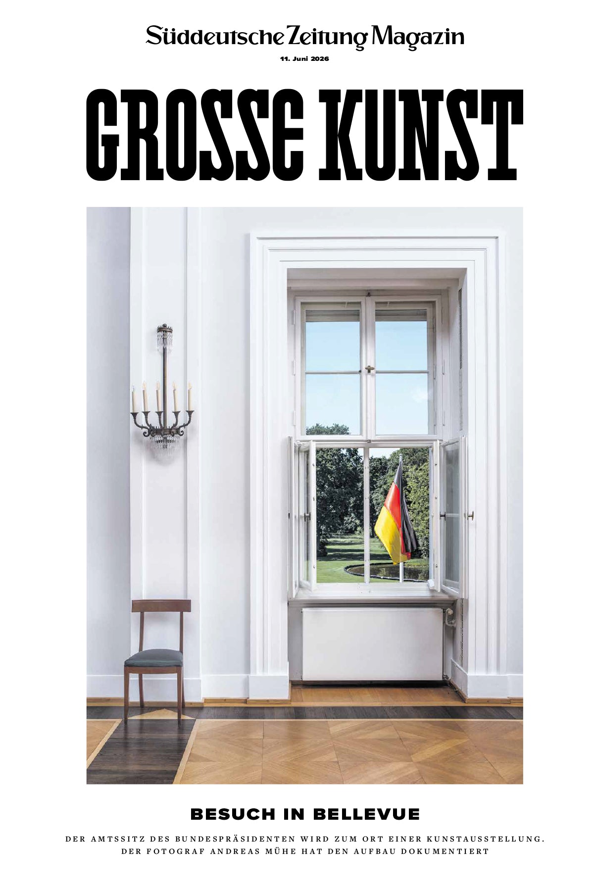 Ein großes Fenster in einem hellen Raum bietet einen Blick auf einen grünen Rasen, auf dem draußen eine deutsche Flagge weht; im Raum sind zwei schwarze Stühle und eine Kerzenleuchte zu sehen.