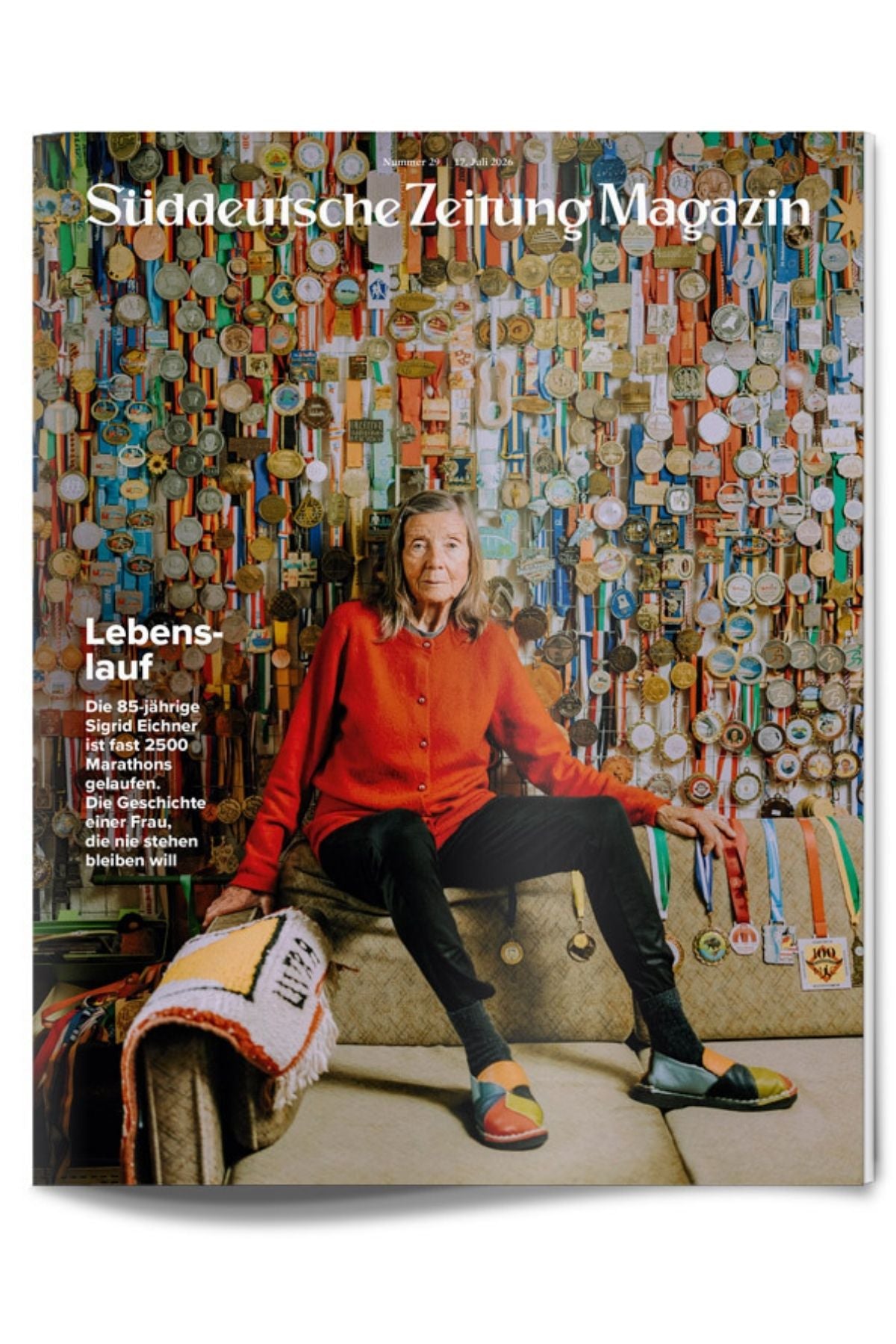 Eine Frau sitzt auf einem Sofa vor einer Wand, die mit Medaillen bedeckt ist. Sie trägt eine rote Jacke und bunte Schuhe. Oben ist der Titel der Zeitschrift „Süddeutsche Zeitung Magazin“ zu sehen.